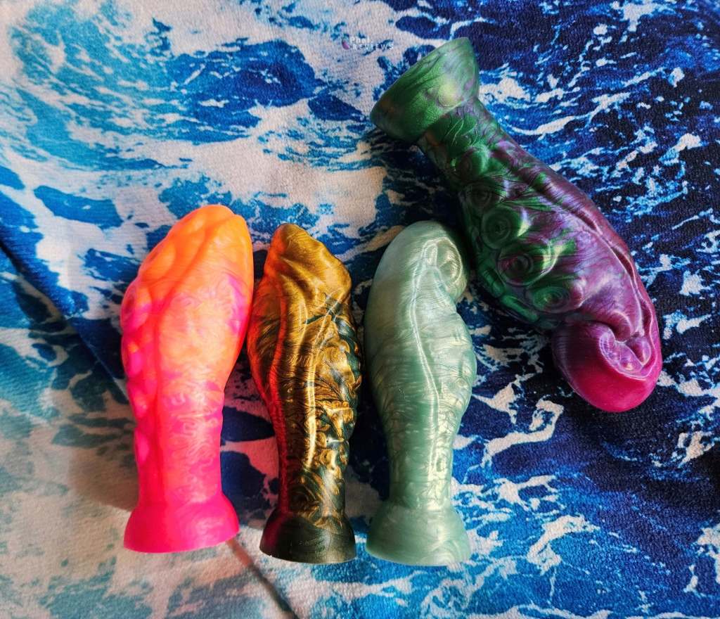 4 Uberrime tentacle plug toys in bright and pearlescent colors, lying flat over wave print background