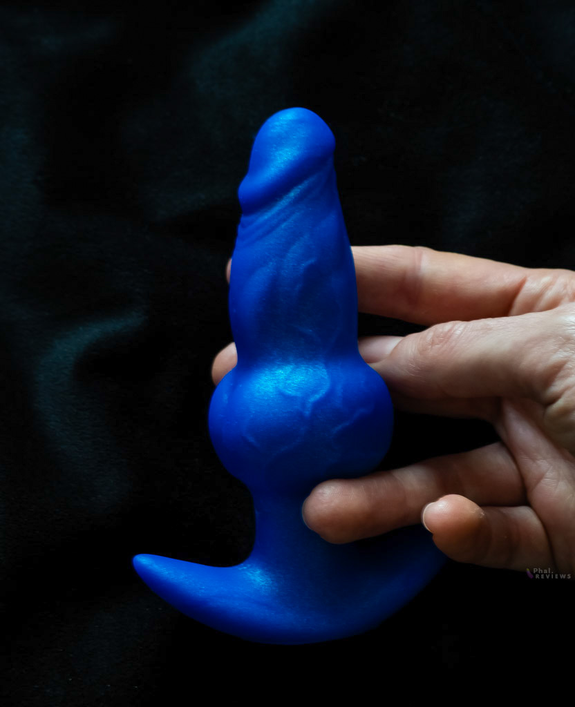 A hand for scale around the Wereknot blue silicone plug over black background