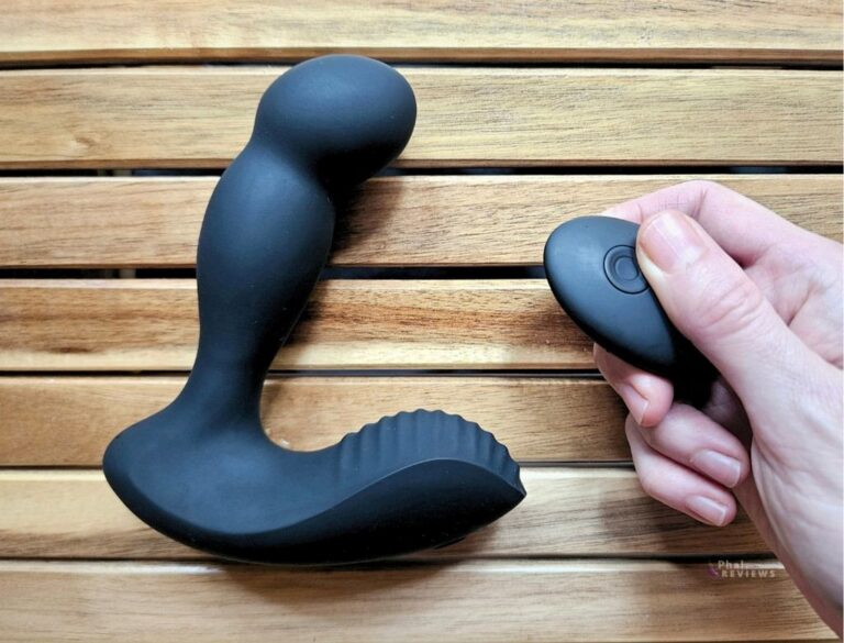 Prostate massager shape with a dramatic curve over a wood background, with remote control in hand to right showing speed-control button with O shape under thumb