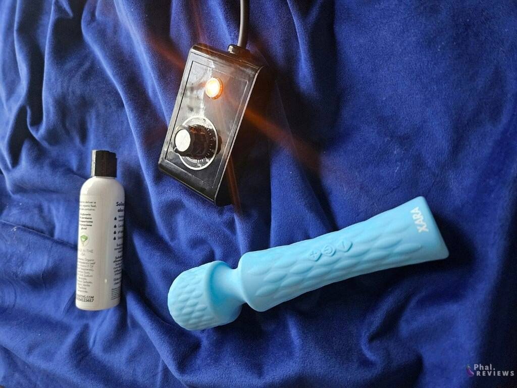 Light blue Speed ​​​​Wand on a dark blue blanket, next to the sex machine controller and bottle of lubricant