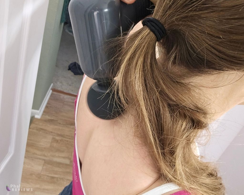 Gray and black massage gun held up and applied to neck, blond ponytail in front