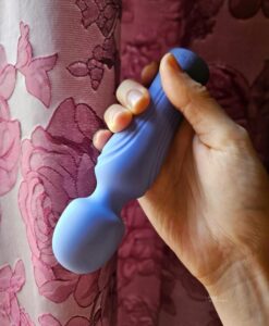 Swan Era wand pint size wand vibrator held in front of open rose print curtain