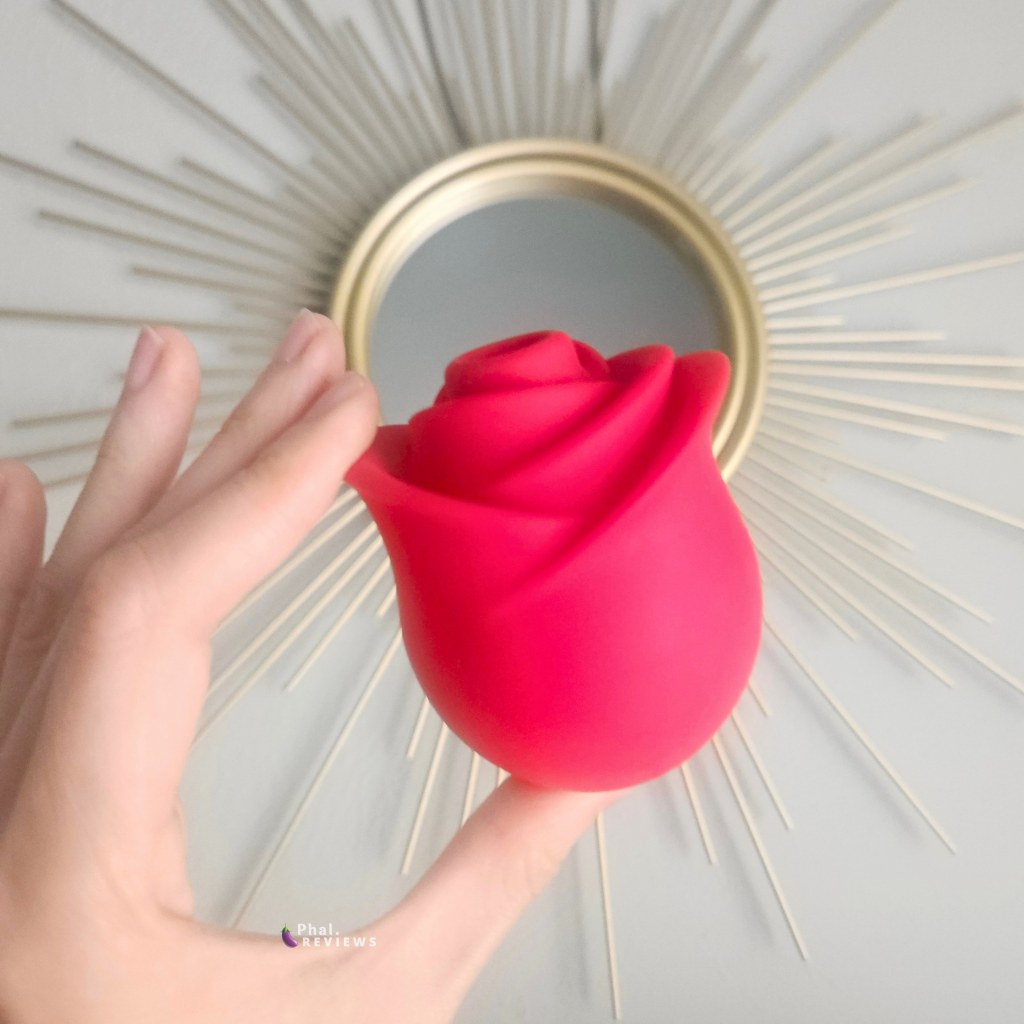 Zen Rose vibrator clitoral toy held in hand in front of sunburst mirror